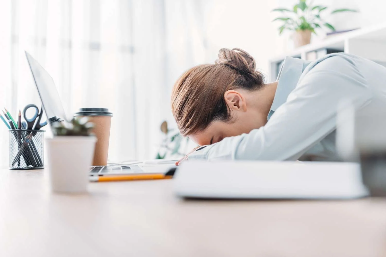 Does Anxiety Make You Tired? Woman feeling exhausted at work due to anxiety-related fatigue and mental exhaustion sitting beside a laptop desk setup