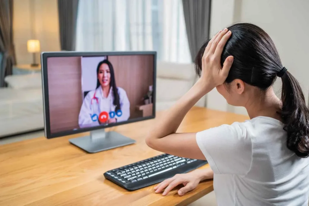 Woman experiencing stress during an online OCD treatment session while speaking with a psychiatrist via telehealth video call on a computer screen.