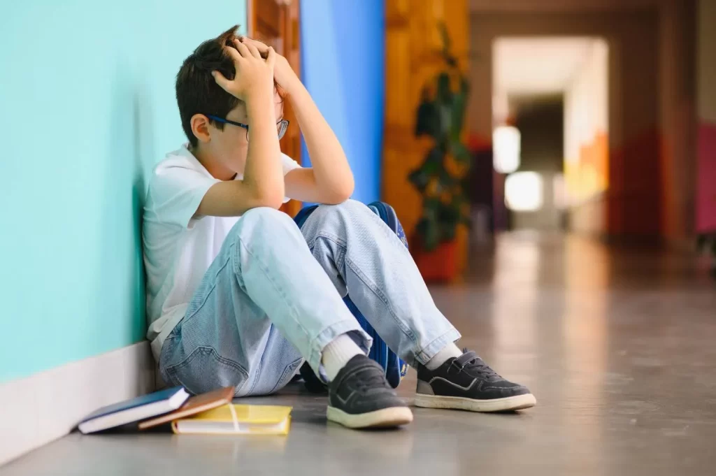 Teen Mental Health News – teen boy sitting alone in school hallway showing signs of anxiety and depression