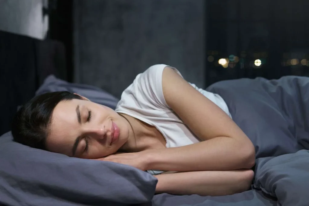 Woman sleeping peacefully in bed at night on her side showing how a good night's sleep benefits your digestion