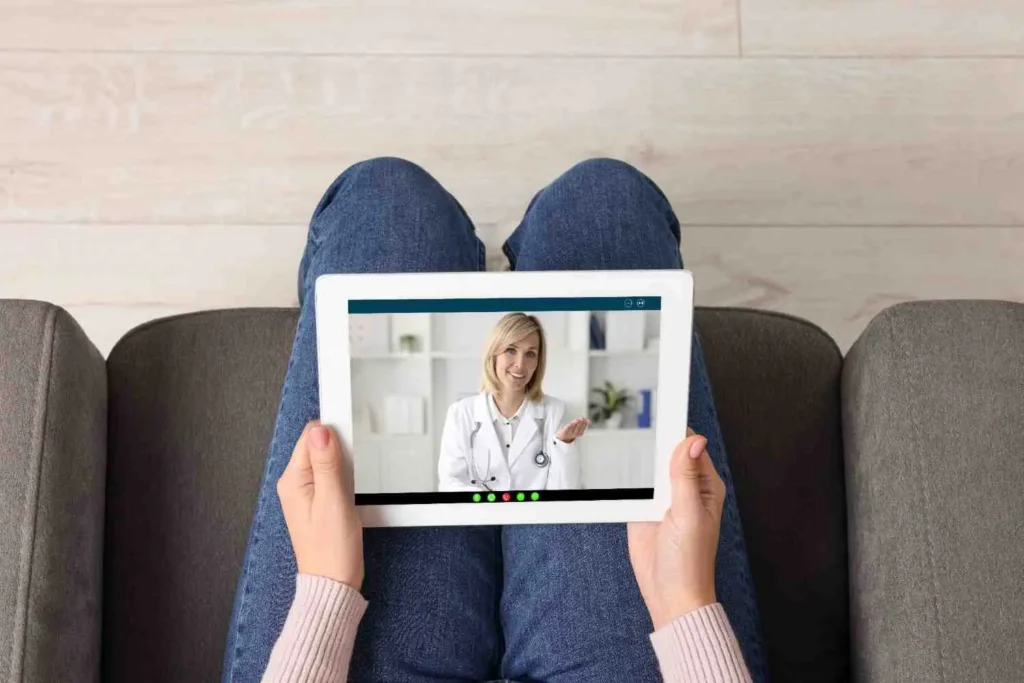 How Does Online Psychiatry Work? A patient sitting on a couch holding a tablet during an online psychiatry video consultation with a licensed psychiatrist